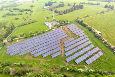 Luftbild des Solarparks in hügeliger Landschaft, umgeben von Wiesen und Laubbäumen.