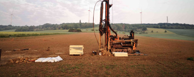 Das Bild zeigt eine Erkundungsbohrung mit einem baggerähnlichen Bohrgerät auf einem Feld