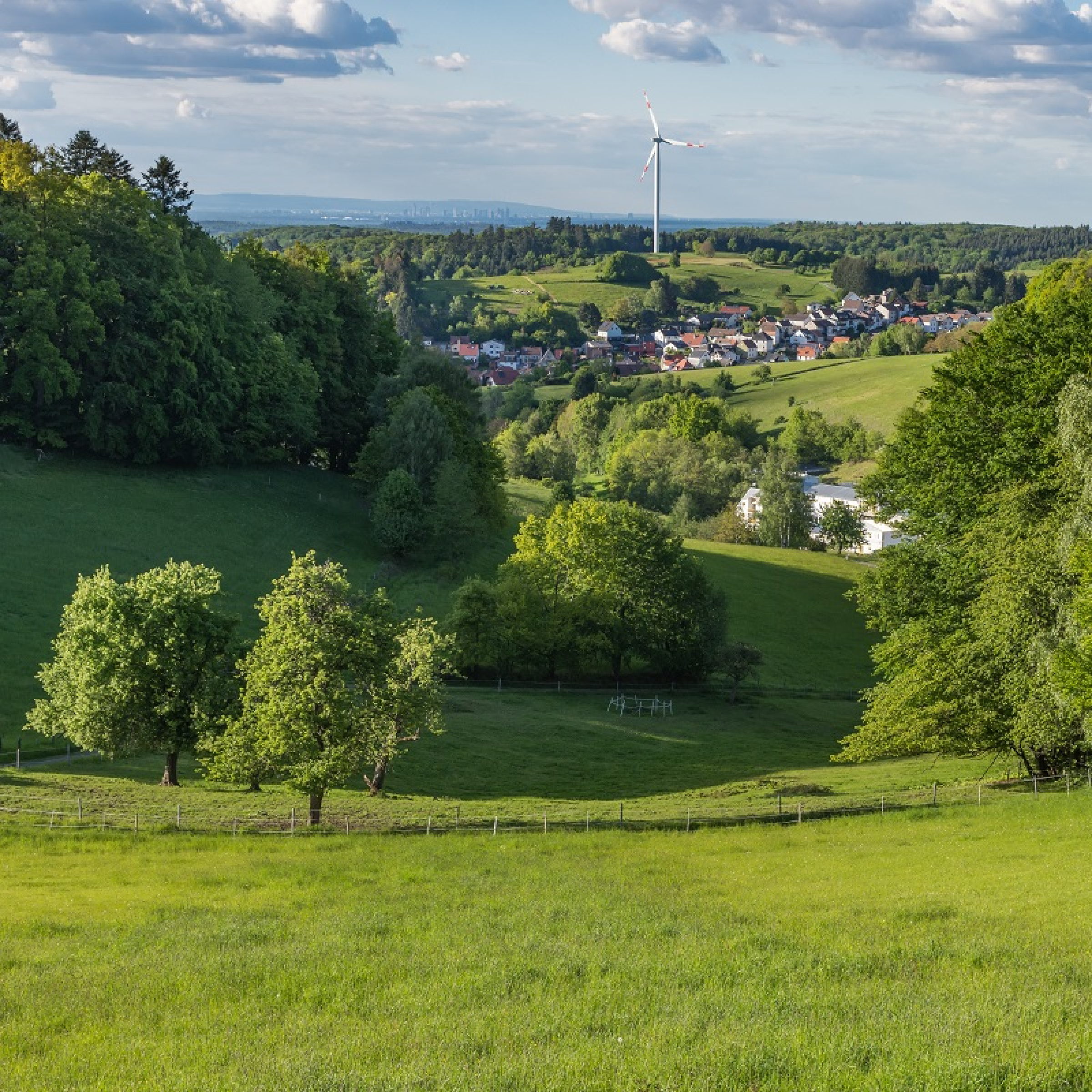 Luftaufnahme einer hessischen Kommune, mit viel gr&uuml;ner freier Fl&auml;che im Vordergrund und zwei Windr&auml;dern im Hintergrund