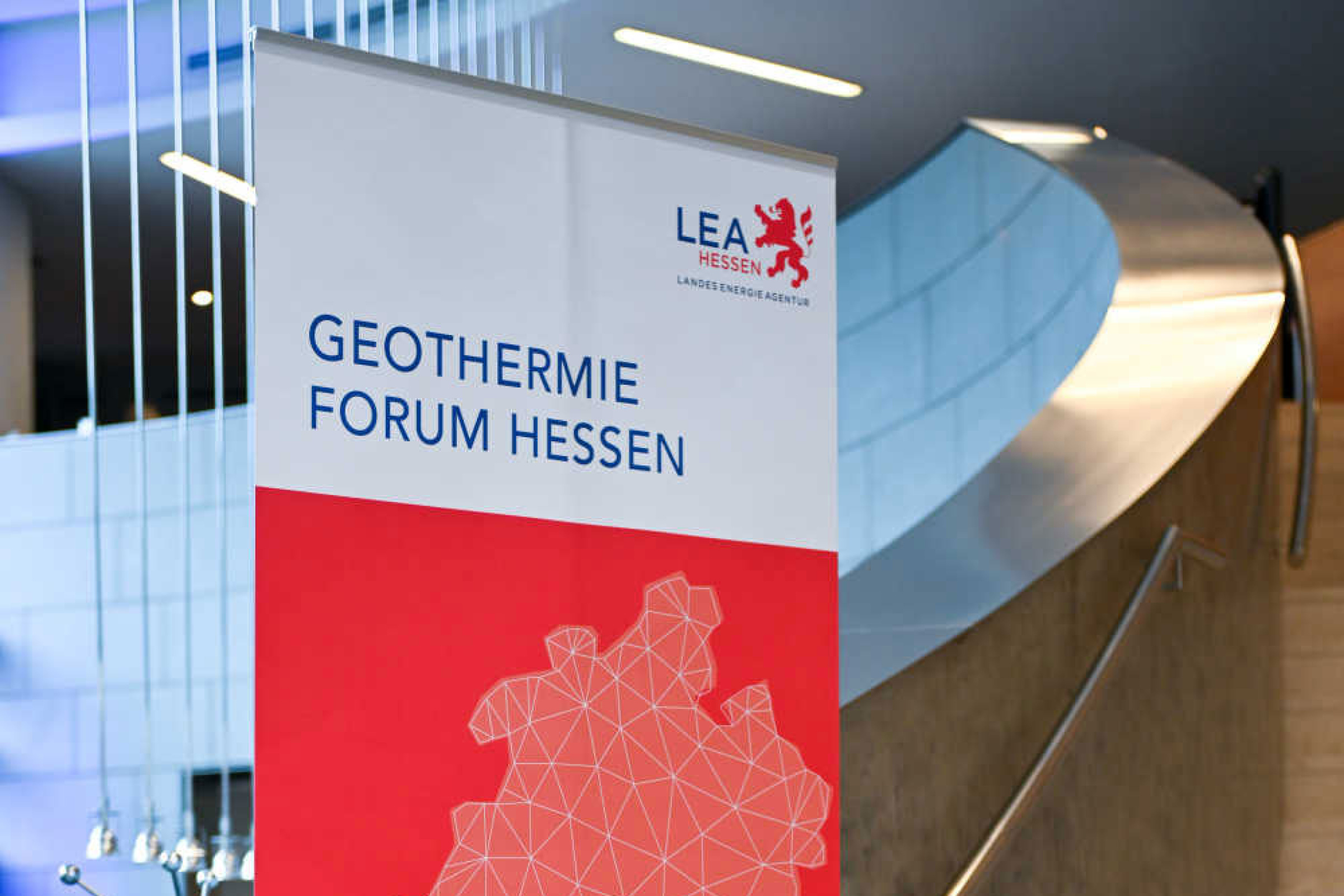Eine rote Stellwand mit der Aufschrift Geothermie Forum Hessen steht am Fuß einer Treppe.