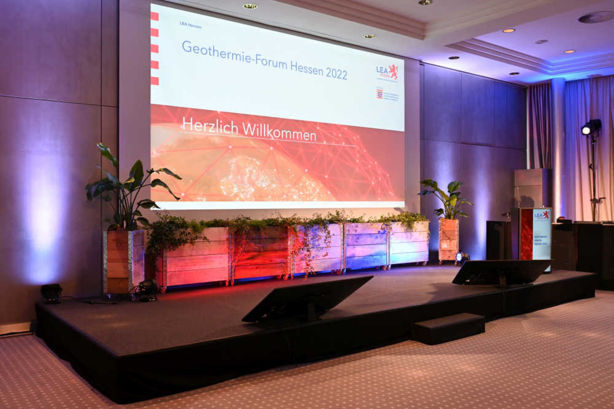 Großbildschirm auf einer Bühn zeigt einen Willkommensgruß, Text: Geothermie Forum Hessen 2022 – Herzlich Willkommen!