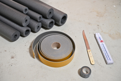 Materialien und Werkzeuge, um die Heizungsrohre in einem Keller zu dämmen.