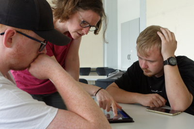 Gruppenarbeit zeigt zwei Schüler und eine Lehrkraft bei Arbeit an Tablet