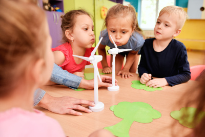 Einige Kindergartenkinder sitzen an einem Tisch und pusten auf Windrad-Modelle.