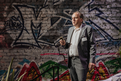 Wärmewende Forum Hessen: Mann im Anzug steht auf der Bühne mit Fernbedienung in der Hand, im Hintergrund Graffiti an einer Mauer.