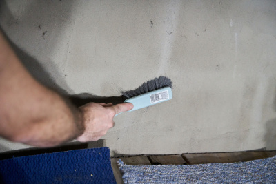 Hand reinigt einen Dachboden mit einem Handfeger.