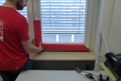 Mann prüft, ob die zugeschnittenen roten Teile auf den Fensterrahmen passen.