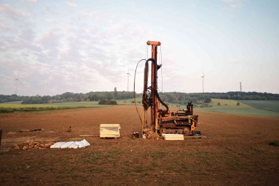 Das Bild zeigt eine Erkundungsbohrung mit einem baggerähnlichen Bohrgerät auf einem Feld