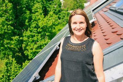Lächelnde Frau auf einem Dach vor einem Solarmodul