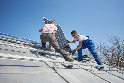 Zwei Handwerker installieren eine Photovoltaikanlage auf einem Dach.