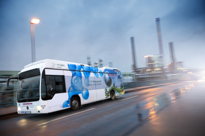 Wasserstoff-betriebener Bus der Firma Winzenhöler fährt auf einer Straße vor einer Fabrik.