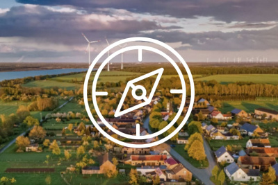 Kompass-Icon vor einem Bild, das eine Gemeinde aus der Vogelperspektive zeigt mit Windrädern im Hintergrund