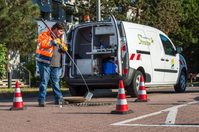 Mitarbeiter der Abwasserüberwachung entnimmt eine Kanalprobe vor seinem E-Auto