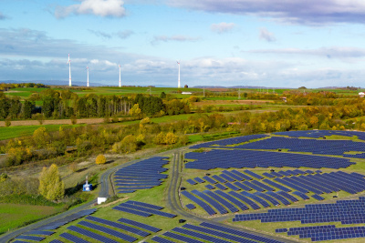 Freifl&auml;chen Solarfeld mit Windenergie im Hintergrund auf H&uuml;geln und Wald im Hintergrund