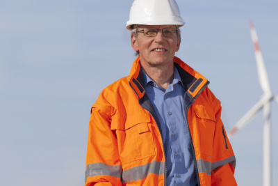 Ingenieur mit weißem Helm stehend vor Windrädern.