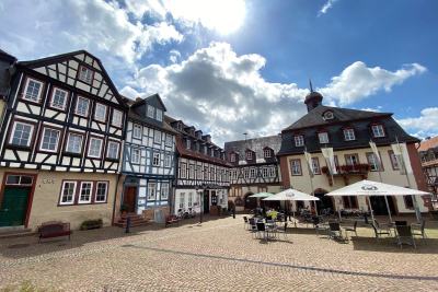 Platz in Gelnhausen mit Fachwerkhäusern, Sonnenschirmen und Kopfsteinpflaster.