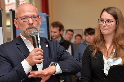 Infomarkt in der Gemeinde Ringgau, ein Mann spricht in ein Mikrofon, eine junge Frau steht daneben.