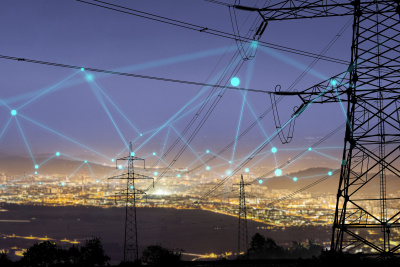 Symbolbild für effiziente Energievernetzung: Strommasten vor einer erleuchteten Stadt, am Himmel sind vernetzte Linien zu sehen.