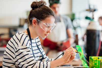 Eine Jugendliche in der Schule trägt eine Schutzbrille und macht Experimente im MINT-Unterricht.