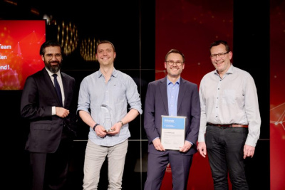 Vier Männer stehen lächelnd auf Bühne, einer hält eine Urkunde, ein anderer einen Preis in der Hand.