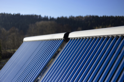 Detailaufnahme von zwei Sonnenkollektoren einer Solarthermieanlage mit Wald im Hintergrund.