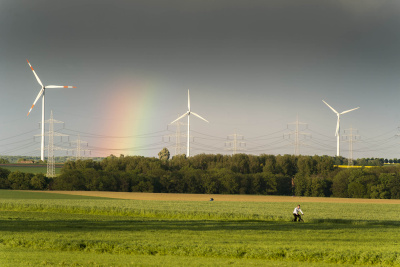 Drei Windräder stehen in einer Naturlandschaft mit grauem Himmel und Regenboden.