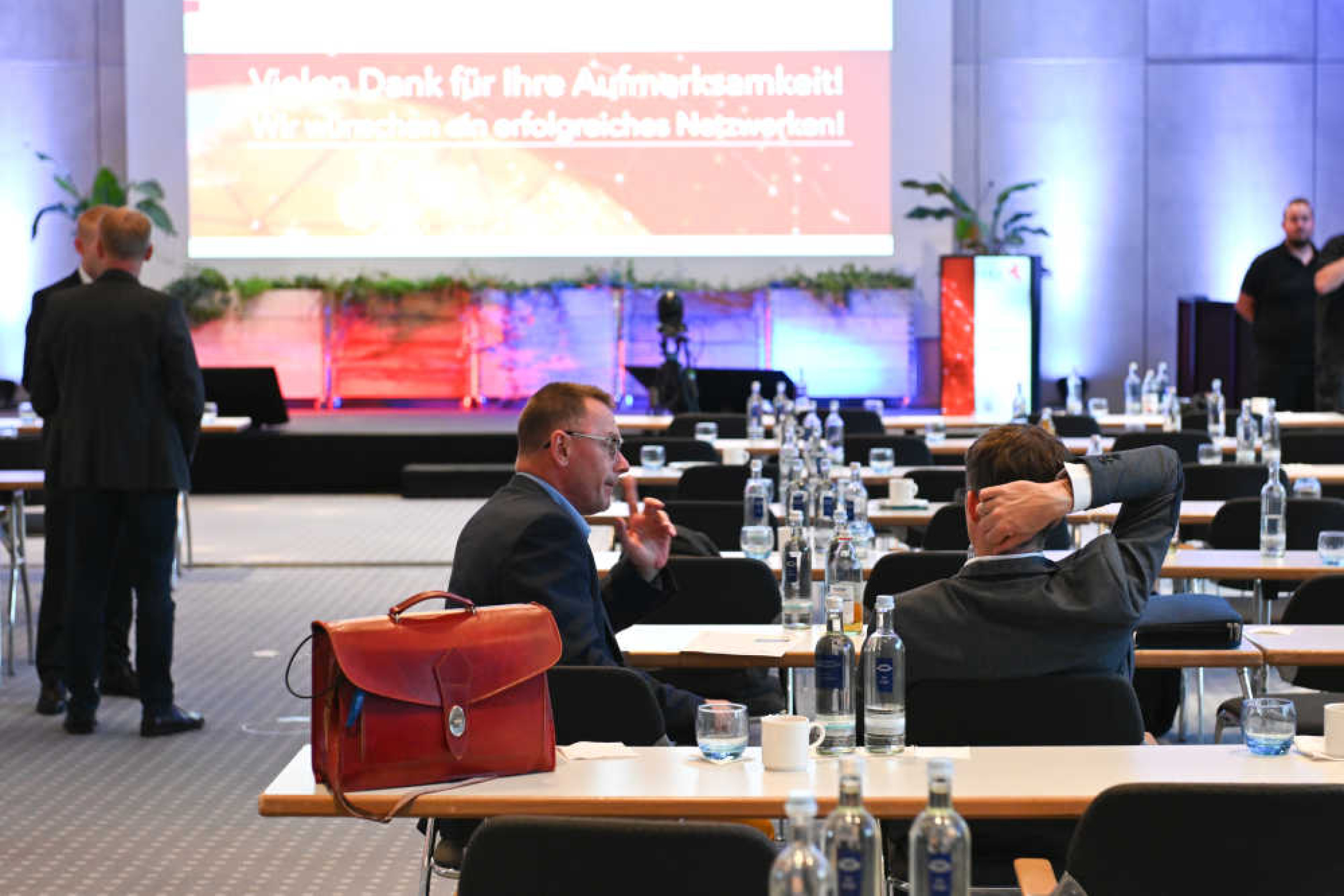 Geothermie-Forum 2022: Pausenimpression Vortragssaal In einem großen Raum sieht man lange Tischreihen, an denen vereinzelt Menschen sitzen oder stehen. Im Hintergrund eine Bühne mit einem Großbildschirm, auf dem "Vielen Dank für Ihre Aufmerksamkeit" steht.