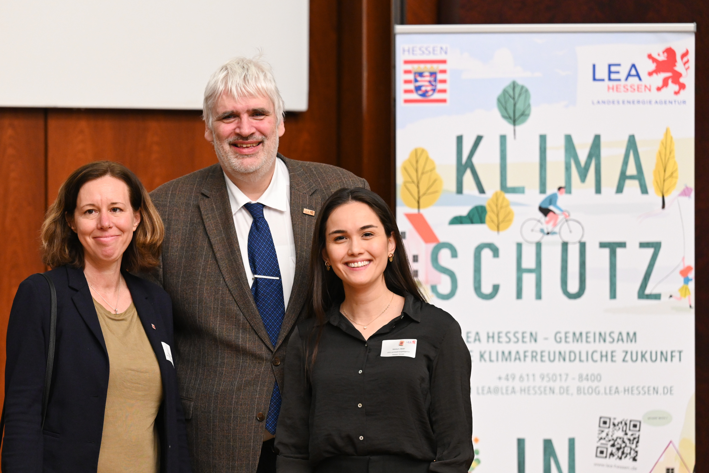 Regionaltreffen IEEKN 2023: Zwei Frauen und ein Mann stehen zusammen auf einer Bühne vor einem Klimaschutz-Poster.