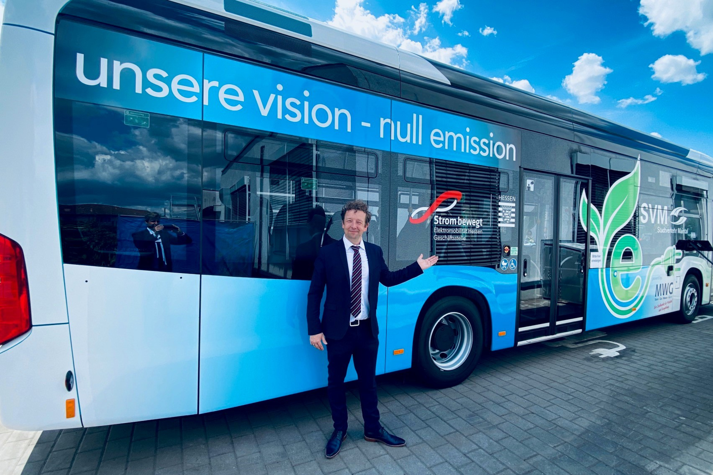 Elektrobus der Gemeinde Maintal steht auf einem Platz und wird betankt. Vor dem Bus steht ein Mann im Anzug.