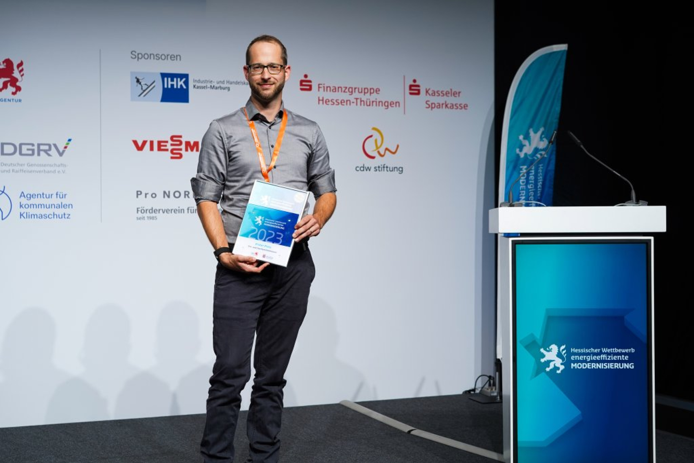 Dr. Patrick Voos steht bei der Preisverleihung auf der Bühne mit Urkunde und Scheck in der Hand.