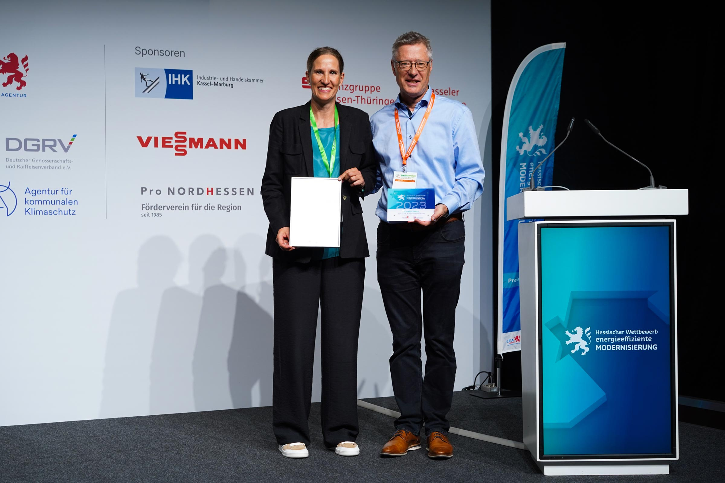 Das Ehepaar Bednarek steht bei der Preisverleihung auf der Bühne und hält Urkunde und Preis-Scheck für den ersten Platz hoch.