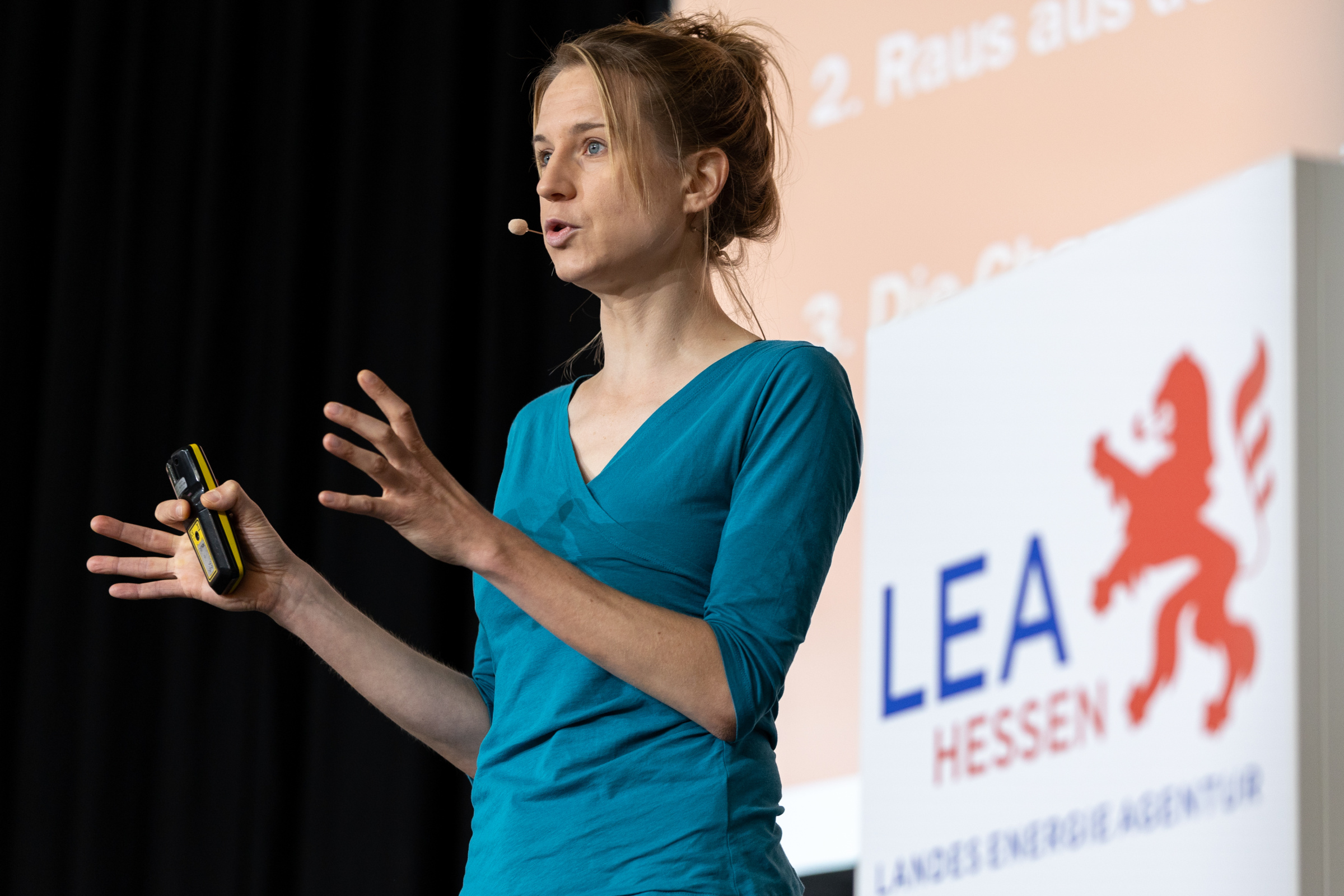 Junge mit Kopfmikrofon und Fernbedienung steht auf einer Bühne, im Hintergrund das Logo der LEA Hessen.