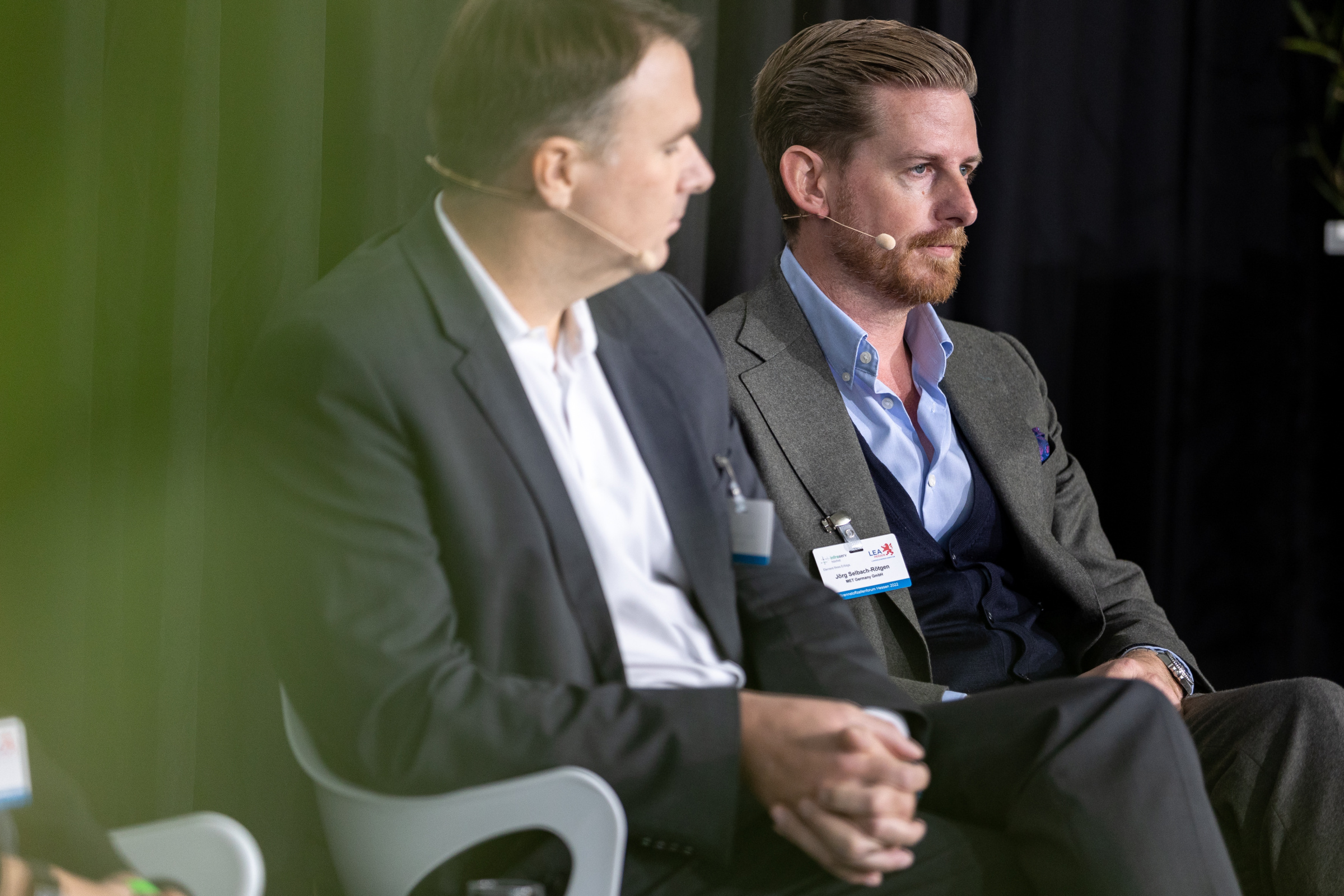 Brennstoffzellenforum 2022 Zwei Männer sitzen mit Kopfmikrofonen auf der Bühne eines Diskussionsforums.
