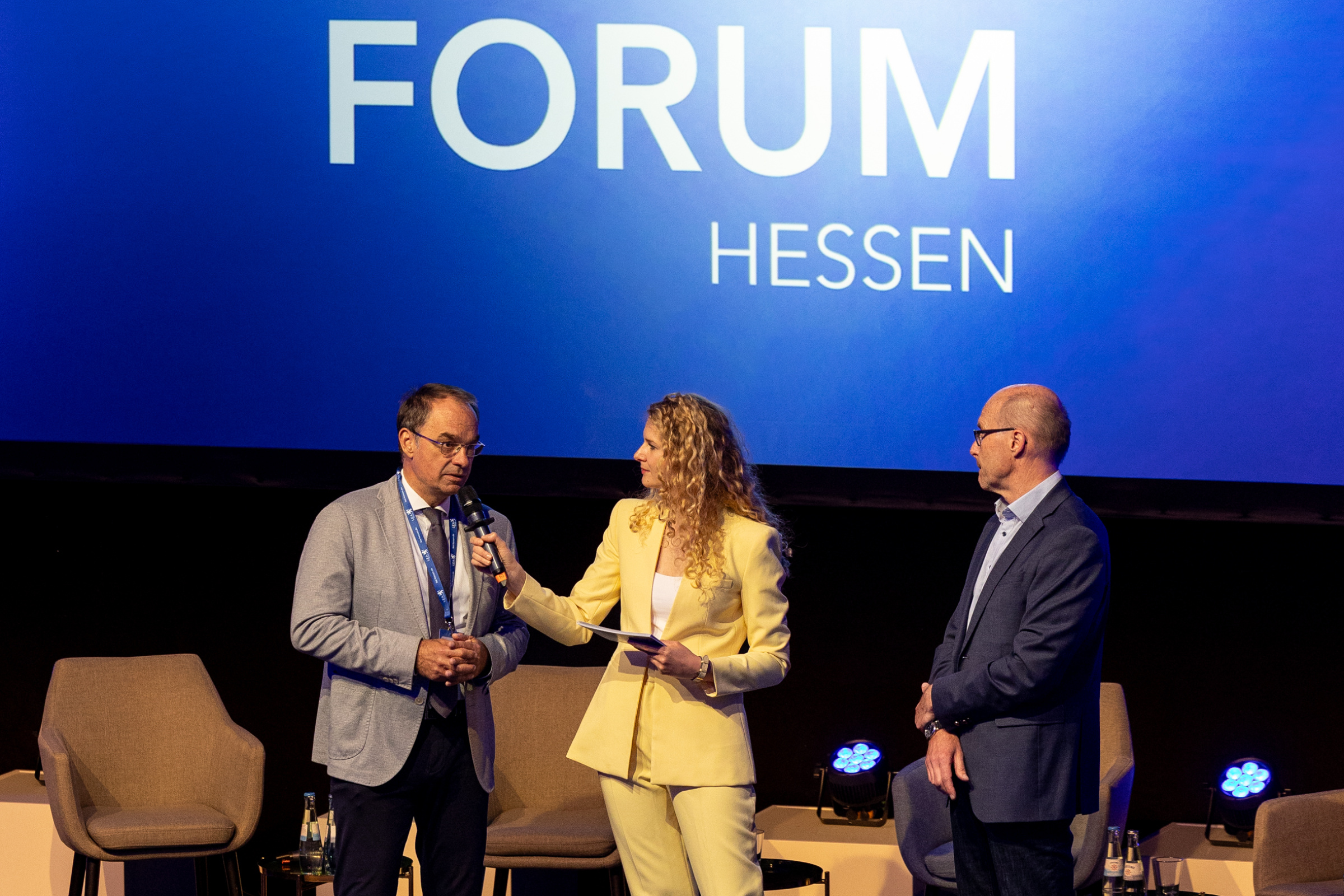 Drei Personen auf der Bühne im Gespräch vor einem Bildschirm mit dem Logo des Wärmwende Forum Hessen