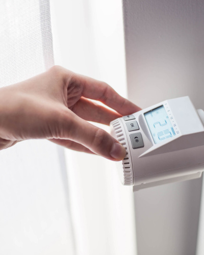 Eine weibliche Hand dreht am digitalen Thermostat einer Heizung