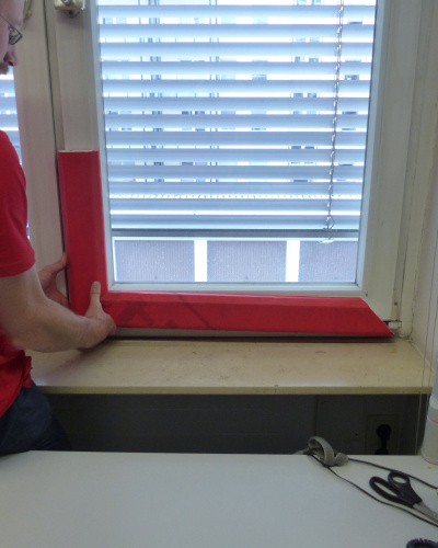 Mann prüft, ob die zugeschnittenen roten Teile auf den Fensterrahmen passen.