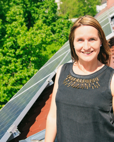 Frau steht auf einer Dachterasse vor einem Solarmodul.