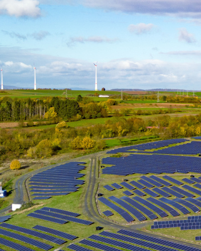 Freiflächen Solarfeld mit Windenergie im Hintergrund auf Hügeln und Wald im Hintergrund
