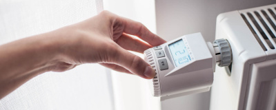 Eine weibliche Hand dreht am digitalen Thermostat einer Heizung
