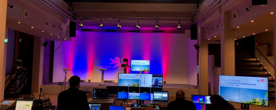 Techniker sitzen mit Bildschirmen und Laptops vor einer Bühne in einem leeren großen Saal.