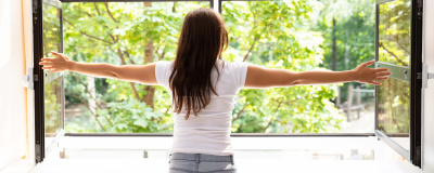 Frau öffnet ein Fenster zum Lüften Eine junge Frau öffnet beide Fensterflügel zum richtigen Lüften ihrer Wohnung