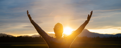 Frau mit hochgereckten Armen im Sonnenuntergang