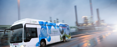 Wasserstoff-betriebener Bus der Firma Winzenhöler fährt auf einer Straße vor einer Fabrik.