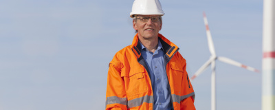 Ingenieur mit weißem Helm stehend vor Windrädern.