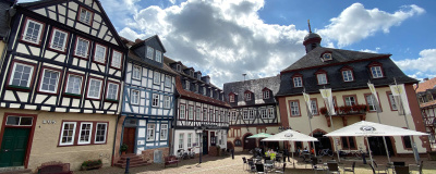 Gelnhausen Platz in Gelnhausen mit Fachwerkhäusern, Sonnenschirmen und Kopfsteinpflaster.