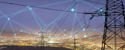 Symbolbild für effiziente Energievernetzung: Strommasten vor einer erleuchteten Stadt, am Himmel sind vernetzte Linien zu sehen.