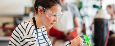 Eine Jugendliche in der Schule trägt eine Schutzbrille und macht Experimente im MINT-Unterricht.