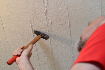 Mann schlägt mit einem Hammer grobe Unebenheiten von der Kellerdecke ab.