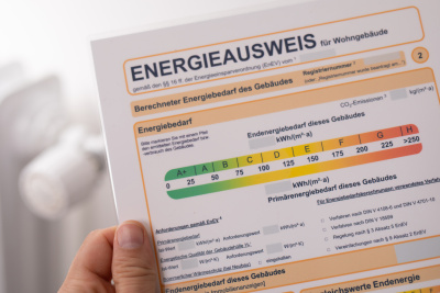 Eine Hand hält einen Energieausweis vor einem Heizkörper.