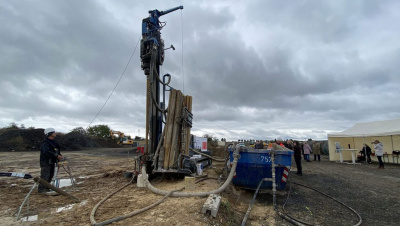 Geothermie Probebohrung: Bohrmaschine mit Arbeiter unter grauem Himmel.